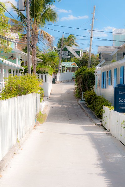 classic impossibly narrow Bahamian street in Hope Town is flanked by white picket fences and walls